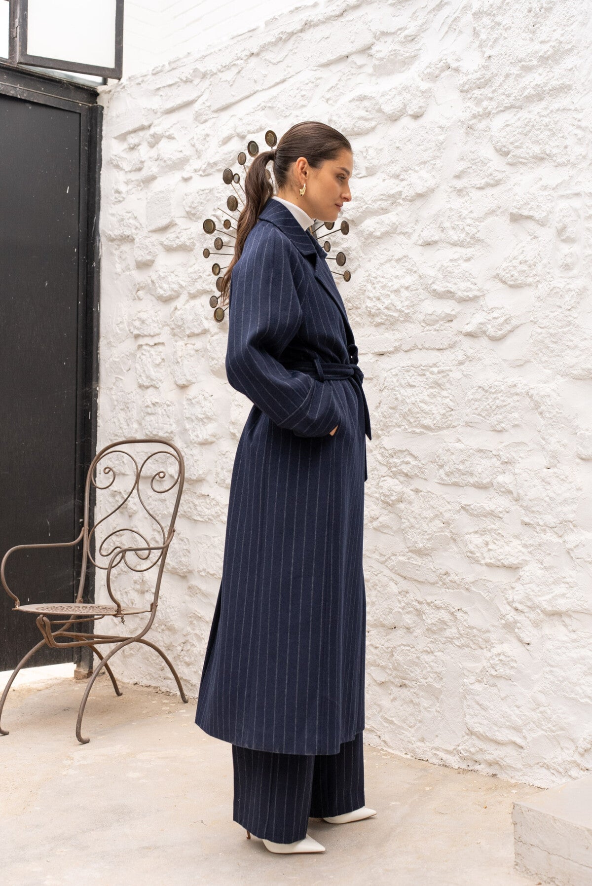Side view of navy long coat with fluid silhouette and dropped sleeves.