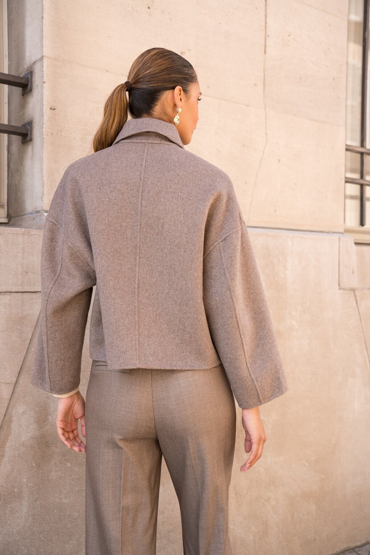 Back view of taupe wool-blend coat highlighting modern cropped silhouette.