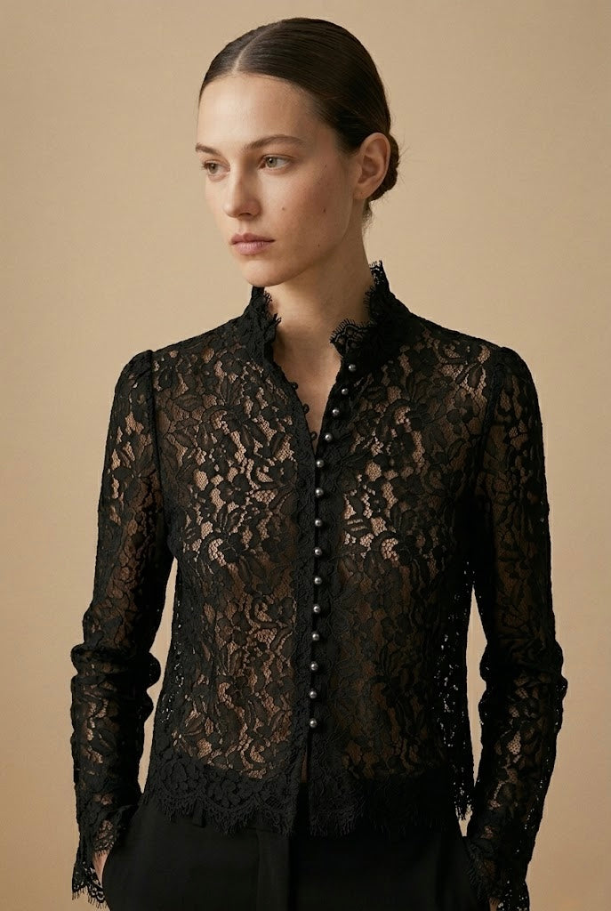 A woman wearing a black lace long-sleeve button-front blouse with a high ruffled collar, photographed against a plain warm beige studio background.