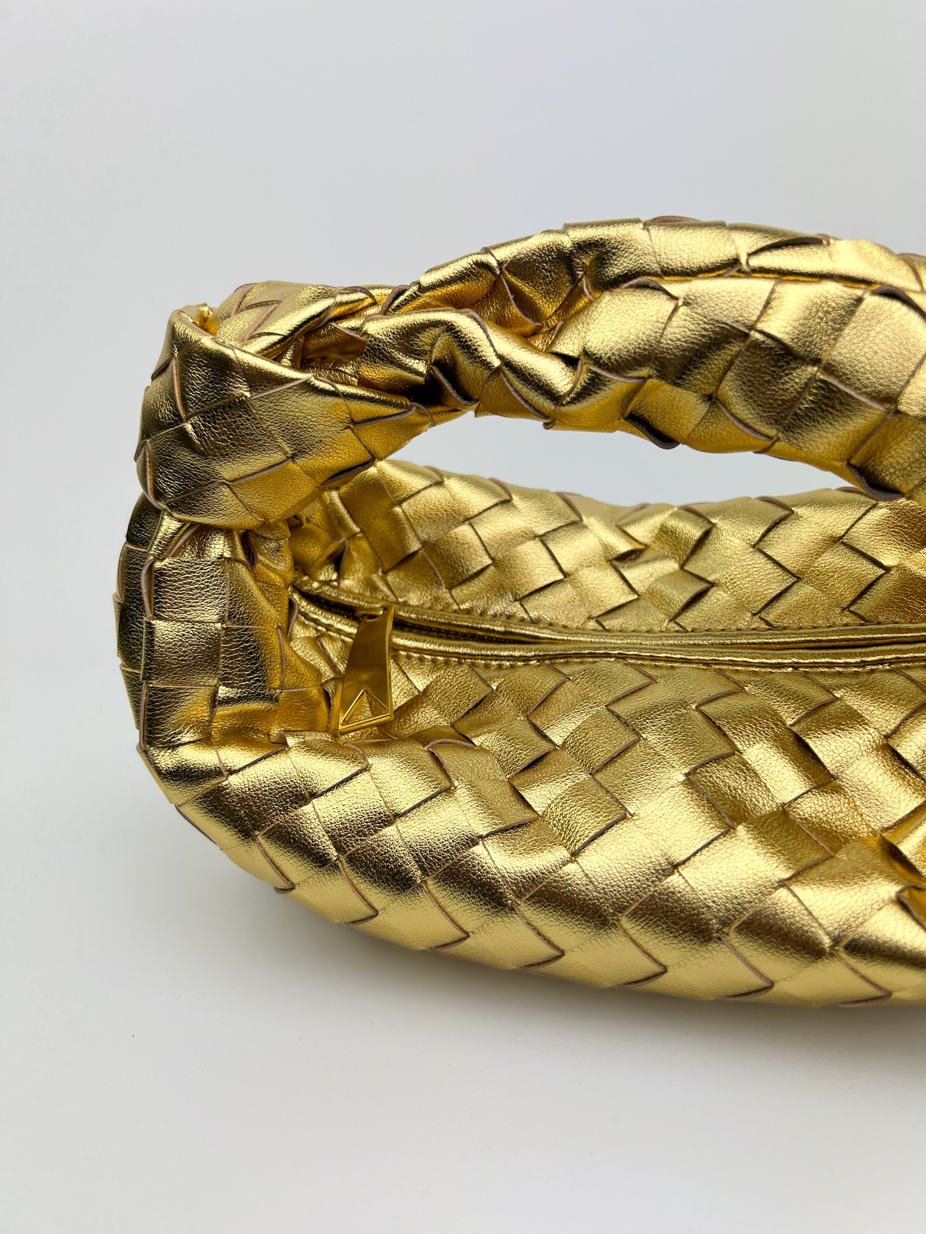 Side view of structured gold leather crescent bag with sculptural silhouette and knotted top handle