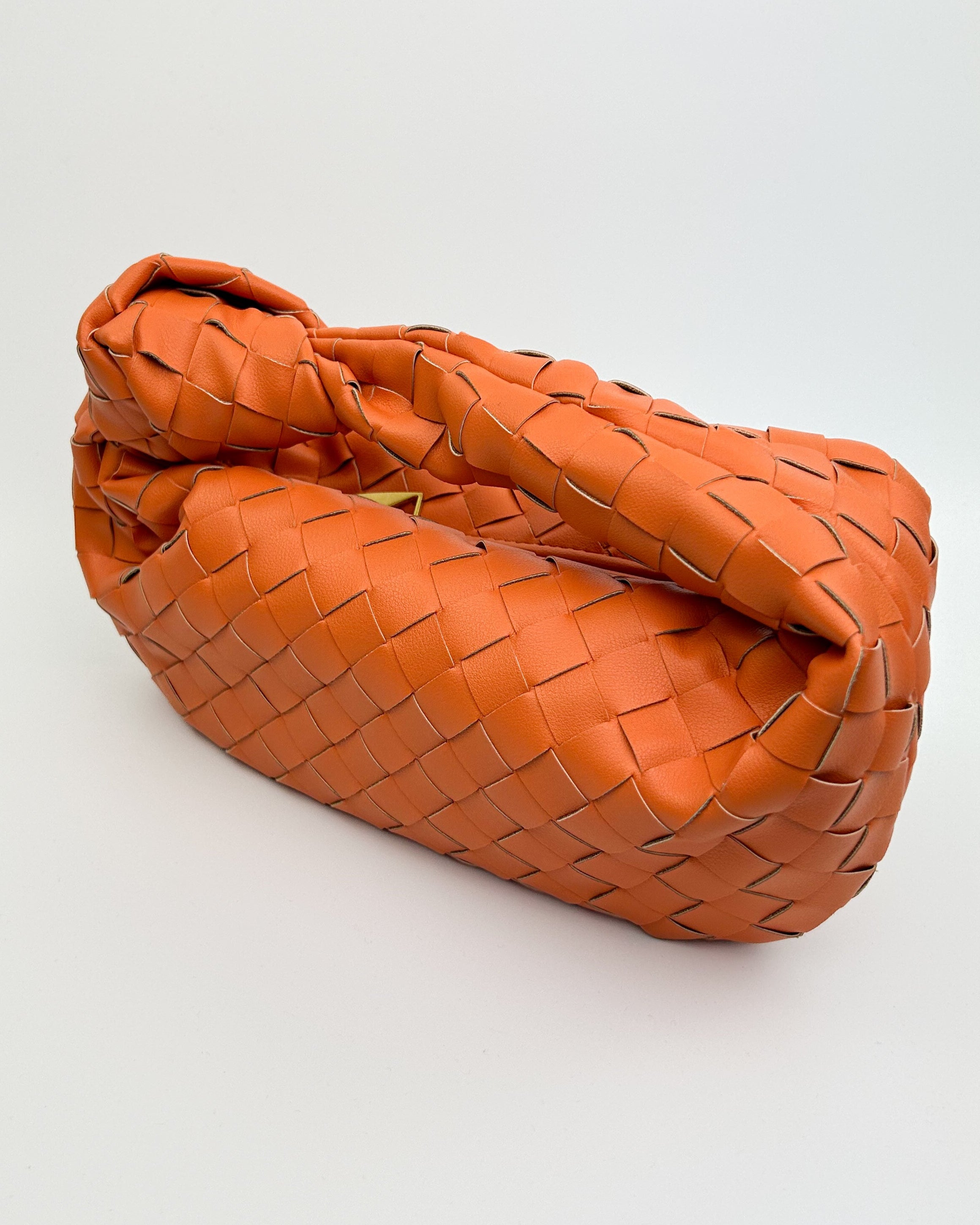 Side profile of orange leather crescent handbag showing sculptural shape and artisan-crafted structure