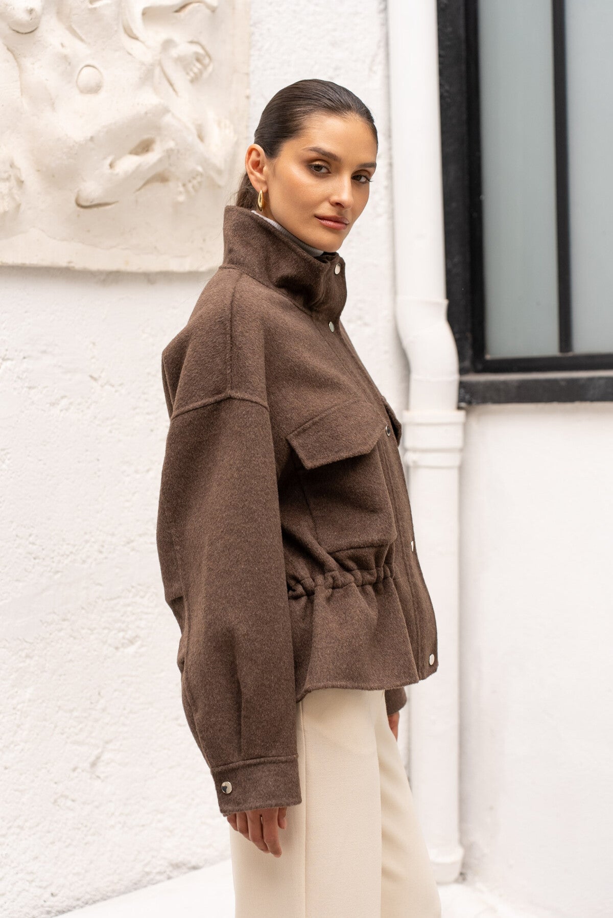 Side view of women’s chocolate coat with elasticated waist and long sleeves.