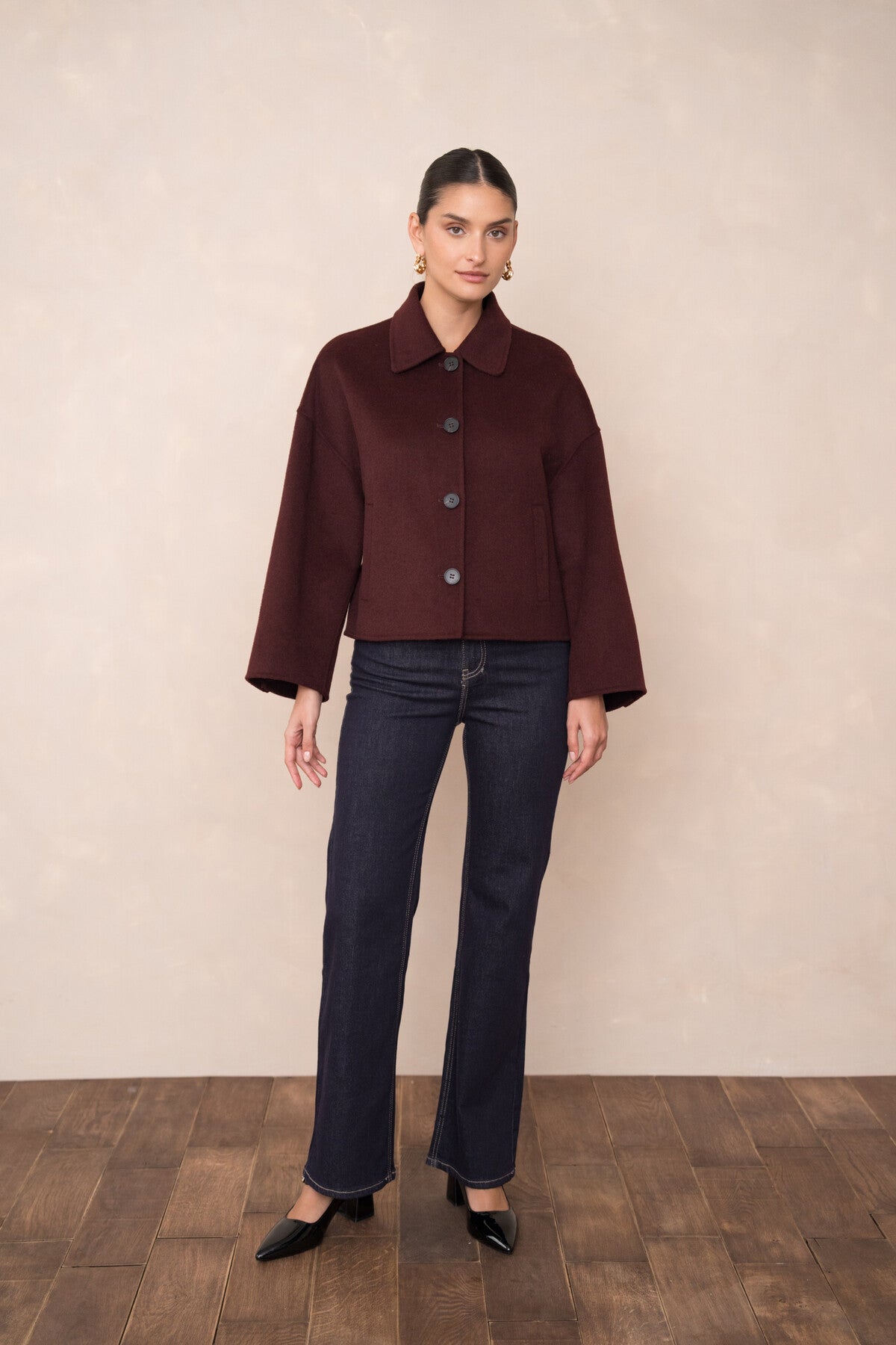 Model wearing burgundy short coat styled with trousers – classic shirt collar visible.