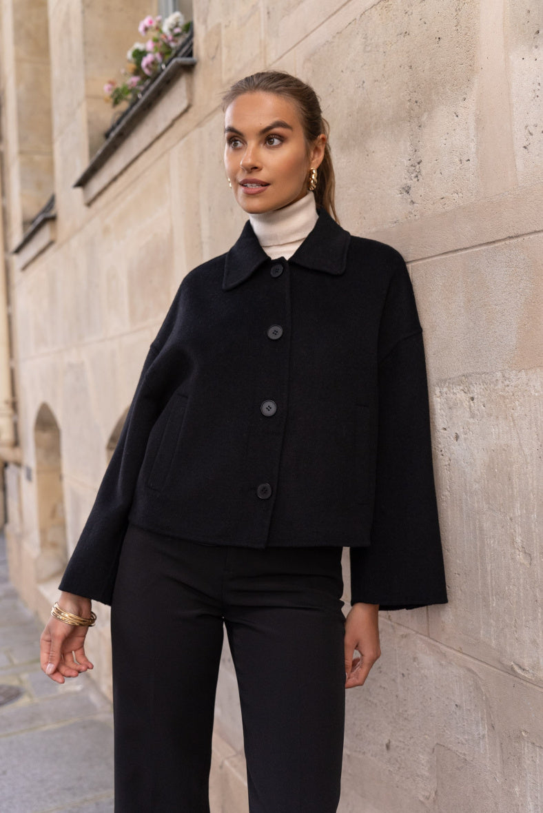 Model wearing black short wool coat with trousers – classic shirt collar visible.