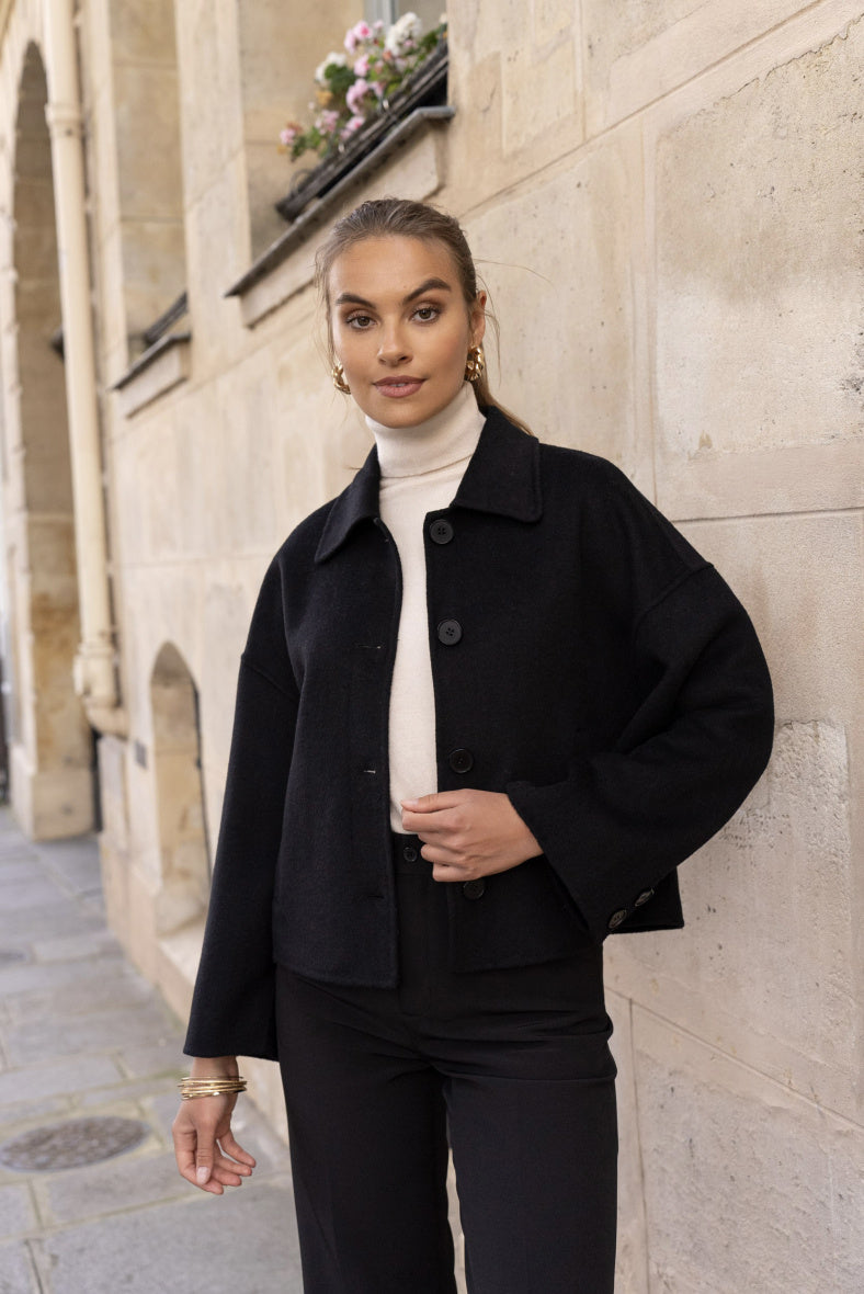 Side view of women’s black wool coat showing discreet pockets and smooth texture.