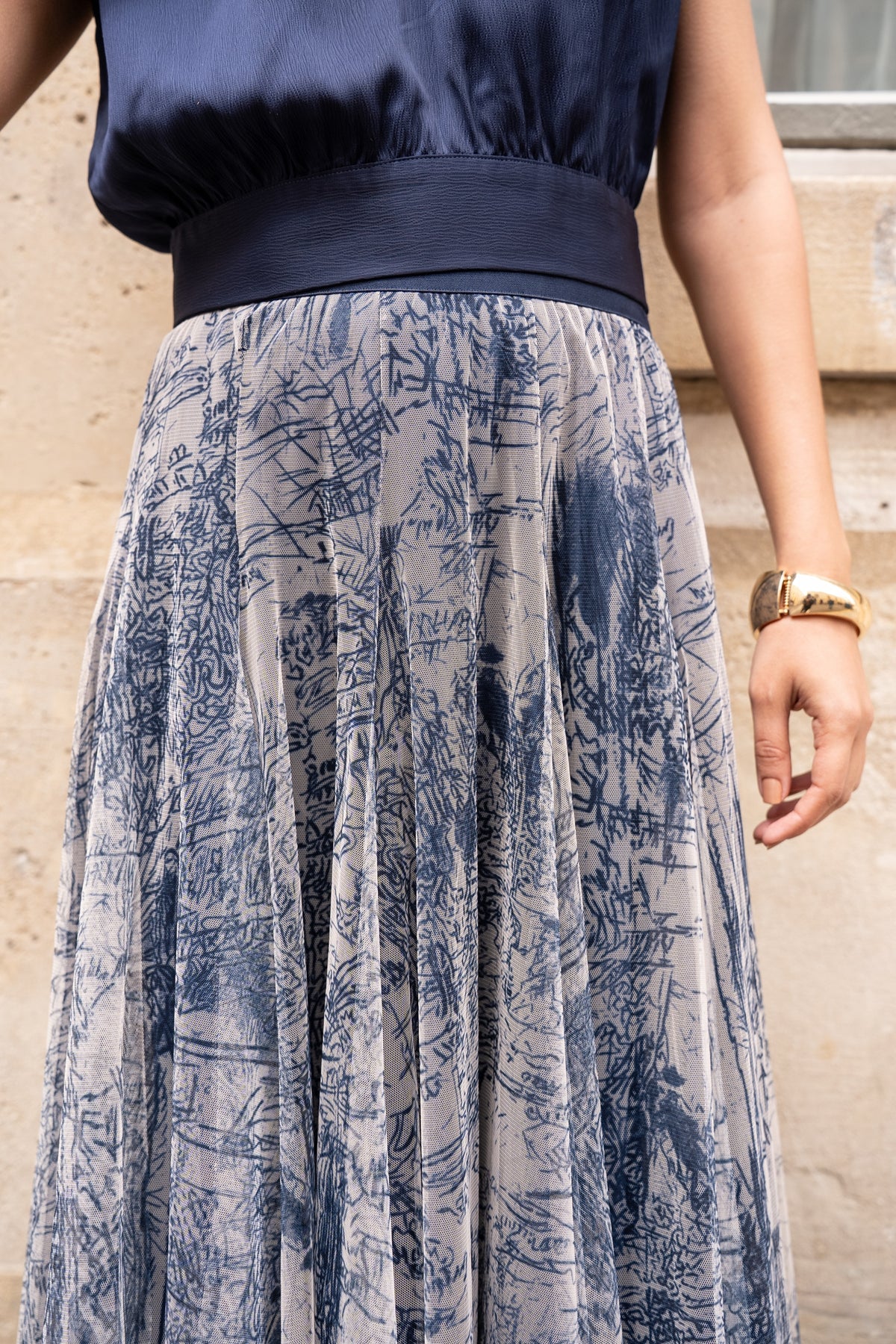 Person wearing a navy top and a long, patterned skirt with a neutral background