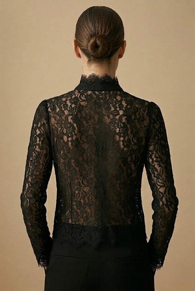 A woman shown from the back wearing a black lace long-sleeve blouse with a high mock neck and lace waistband, paired with black trousers, against a solid beige background.