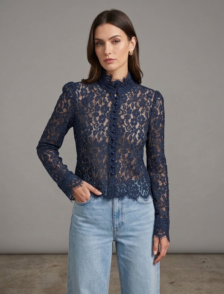 A woman modeling a navy blue lace long-sleeve blouse with a high mock neck and buttoned front, paired with light-wash blue jeans, against a neutral gray studio background.
