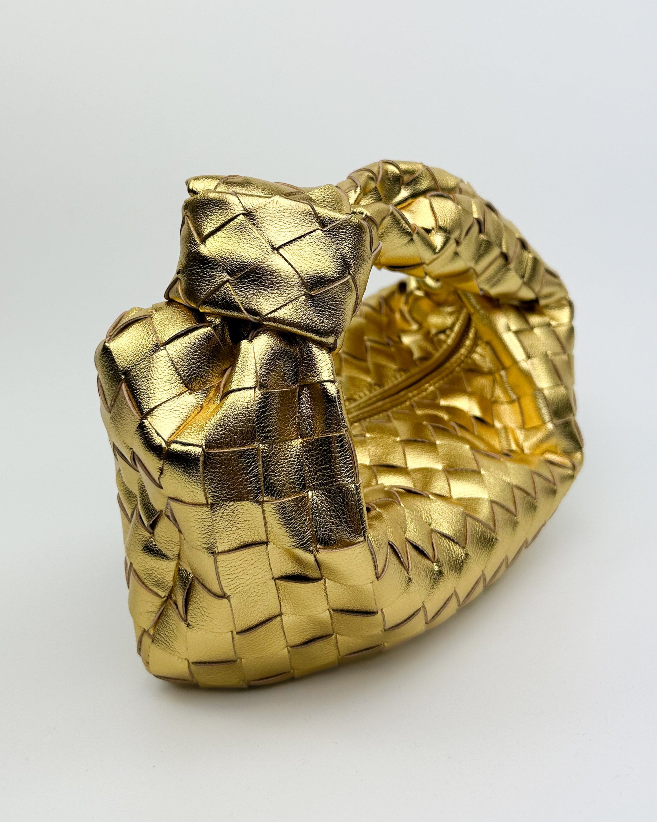 Detailed close-up of woven metallic gold calf leather and knotted handle on luxury Italian handbag