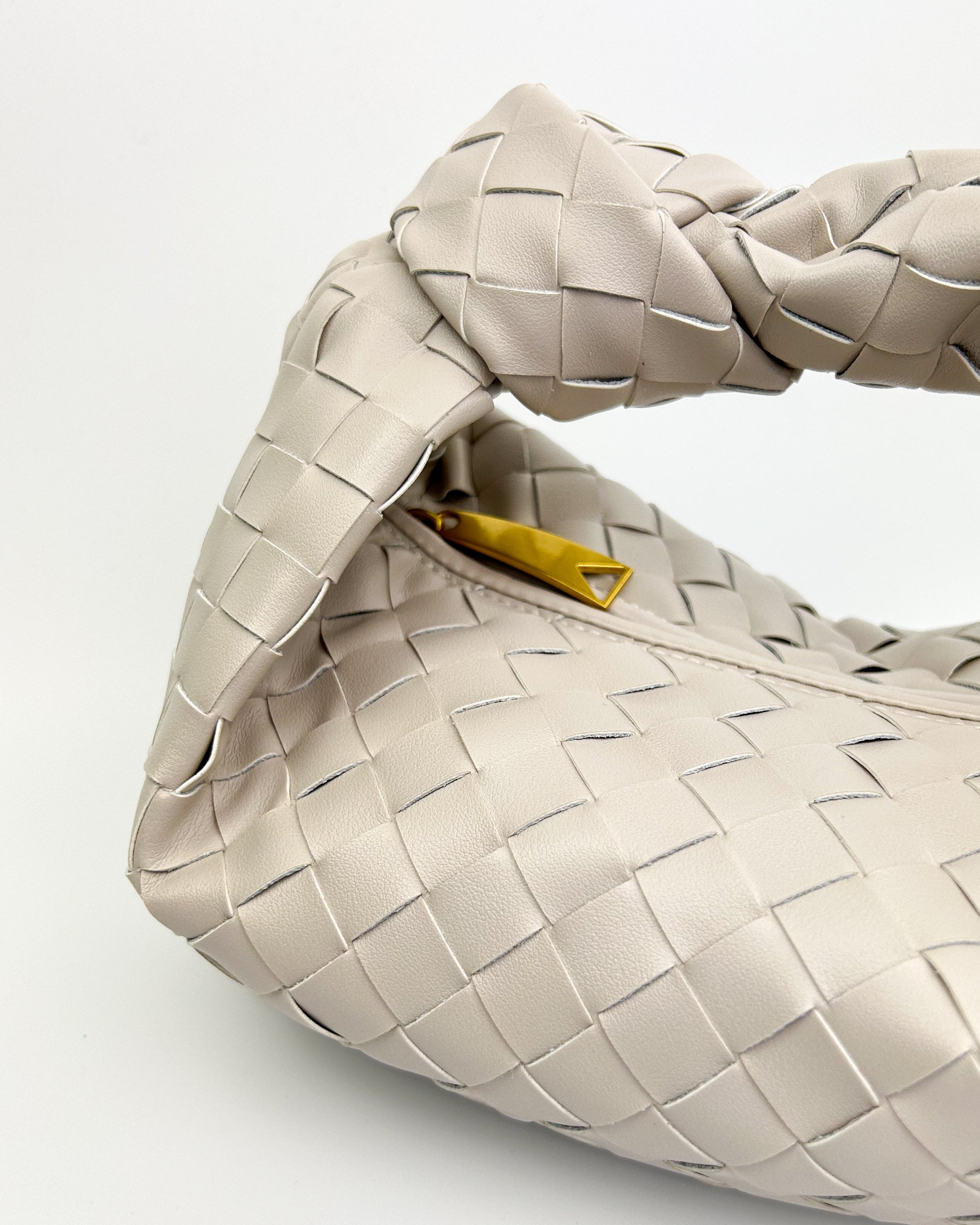 Detailed close-up of woven oyster white Italian calf leather and signature knot handle – luxury handcrafted leather handbag