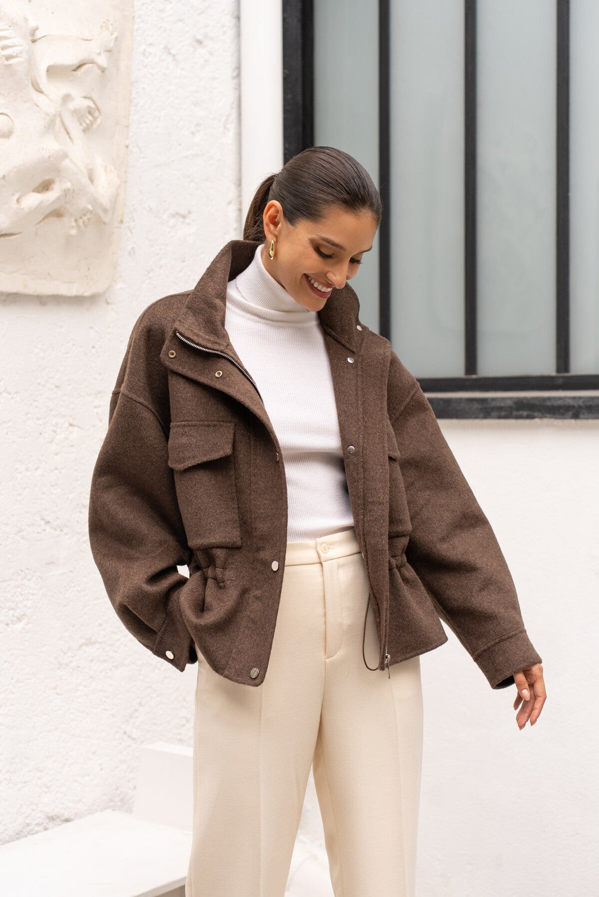 Model wearing chocolate short wool-blend coat with high collar and flap pockets.