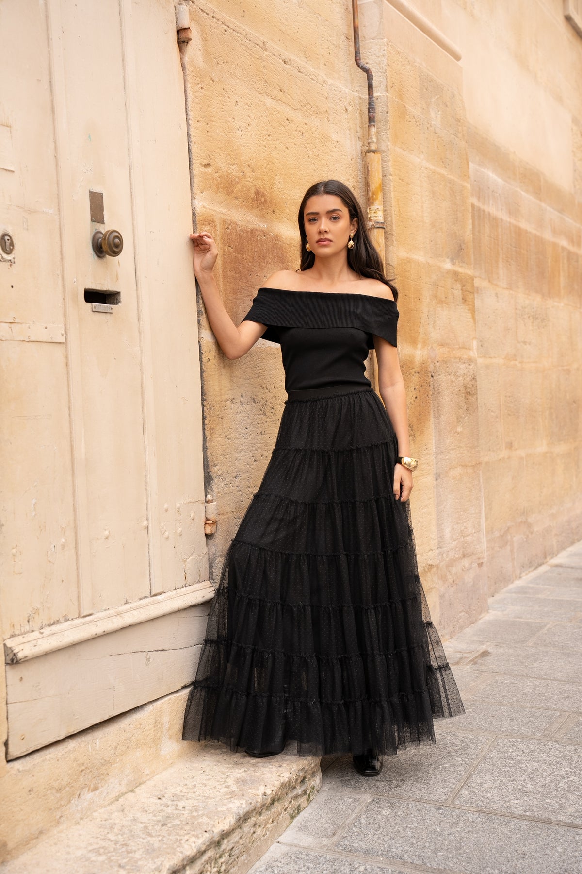 Woman wearing black tiered tulle maxi skirt with black off-the-shoulder top and ankle boots